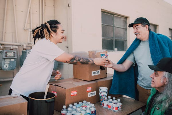 a man with tattoos giving water to homeless people